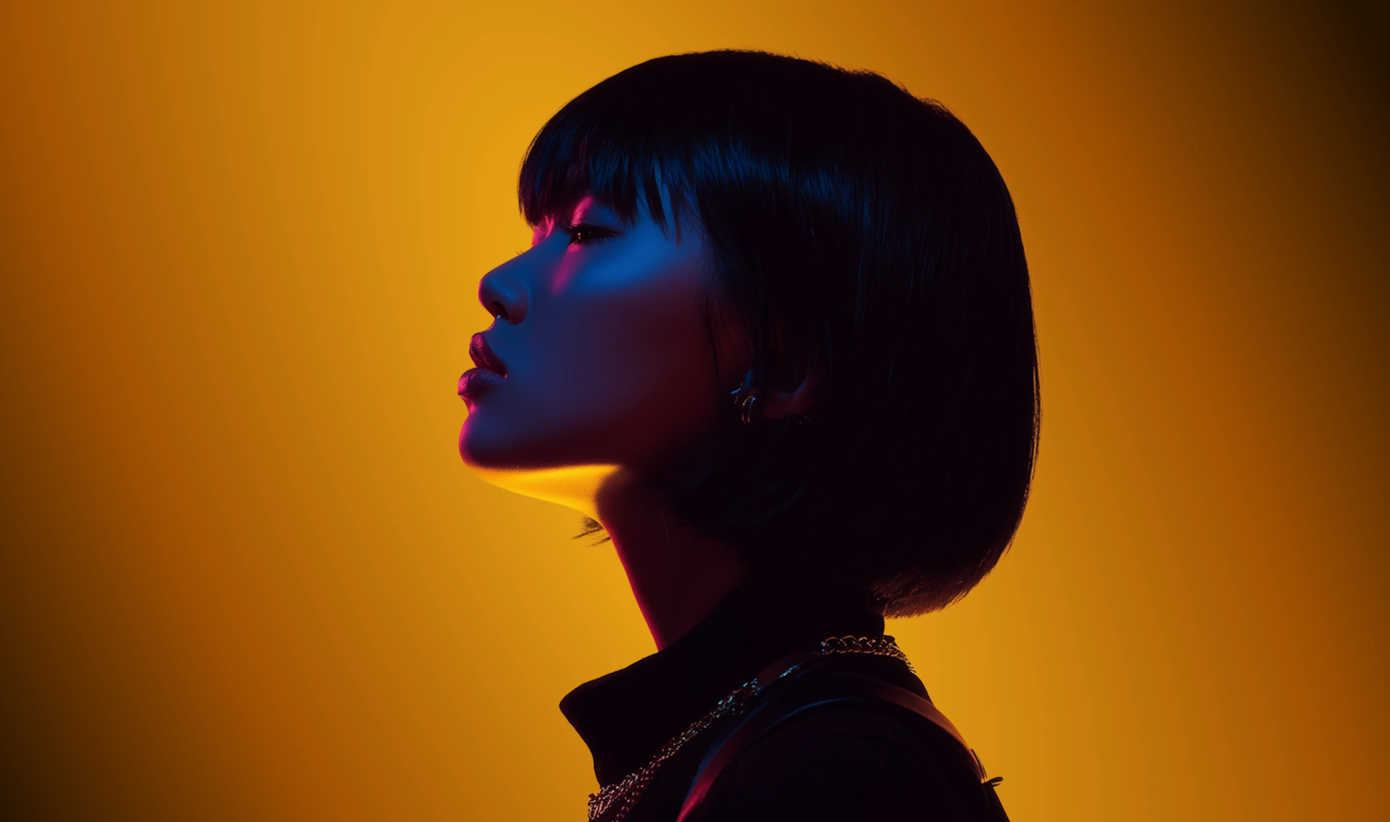 Profile of a woman with short black hair softly illuminated in blue and pink light against a warm yellow background.