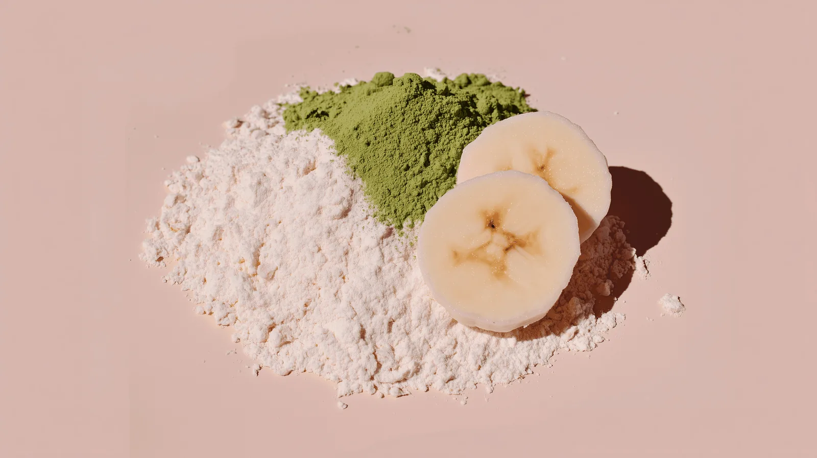 Panda Matcha powder, protein powder and banana slices arranged on a blush pink background