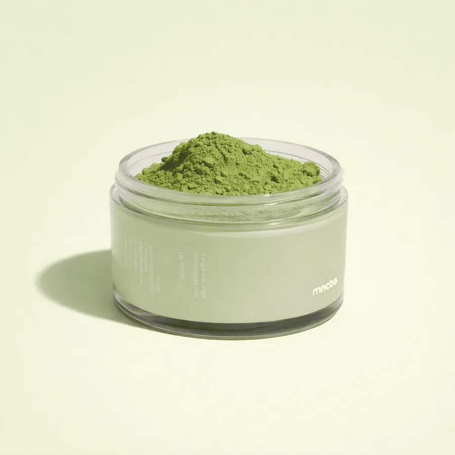 Open ceremonial matcha tin filled with bright green matcha on a pale green background